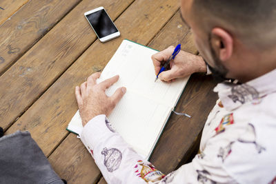 Young bearded businessman sitting at table, making notes in notebook