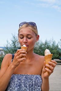 Woman licking ice cream on street against sky