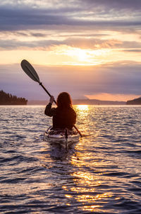 Rear view of silhouette person in sea against sky during sunset