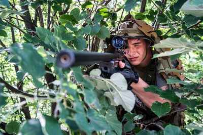 Soldier holding gun by trees in forest
