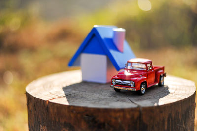 Close-up of toy car by model home on tree stump