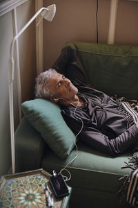 Senior man listening music through in-ear headphones while lying on sofa at home