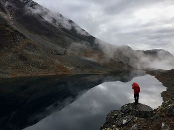 Rear view of man standing on rock against cloudy sky