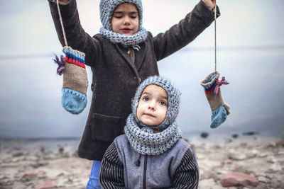Girl in knitted grey hat sharing gloves with her frozen brother