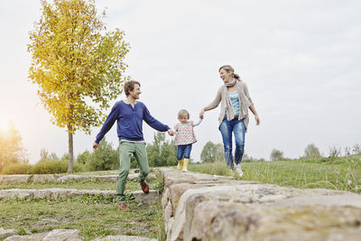 Girl balancing on a wall supported by parents