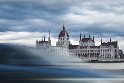 Hungarian parliament building in city against cloudy sky