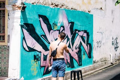 Full length of young man standing against graffiti wall