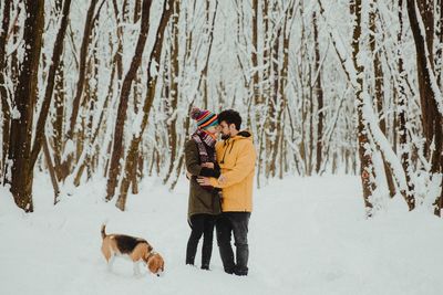 Couple in love with a beagle dog standing in forest during winter
