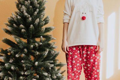 Anonymous female in christmas pajama near coniferous tree at home