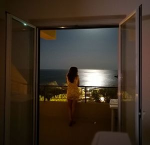 Rear view of woman looking through window at home