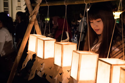 Woman looking at illuminated lanterns hanging outdoors at night