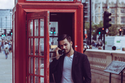 Portrait of businessman talking at telephone booth in city