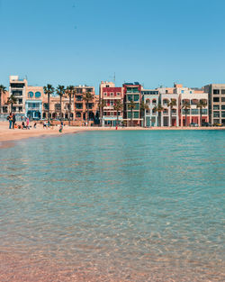 Buildings by sea against blue sky