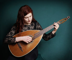 Young woman playing lute against green wall