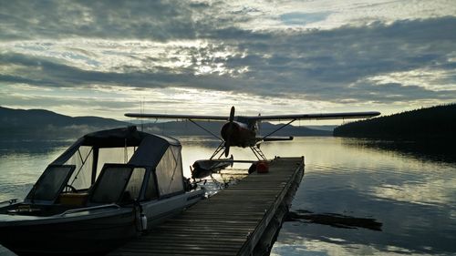 Seaplane and boat by lake against cloudy sky during sunset