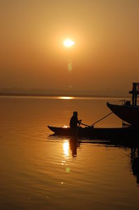 Silhouette man riding boat against sky during sunset