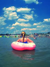 Rear view of young woman sitting in inflatable ring on sea against sky during sunny day