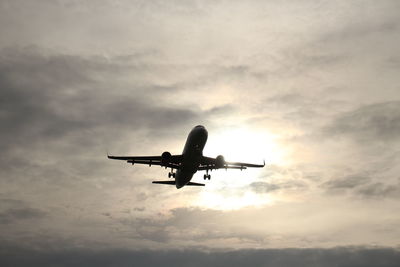 Low angle view of airplane flying against cloudy sky
