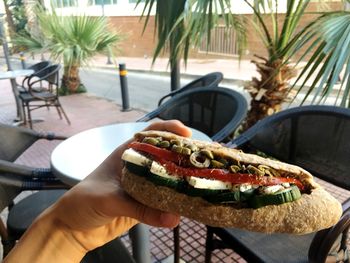 Cropped hand of man having sandwich while sitting at outdoor restaurant