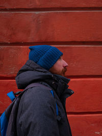 Bearded guy in blue hat coat on red wall background. urban style street photo active lifestyle hiker