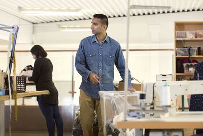 Man standing by plastic container while volunteer working in workshop