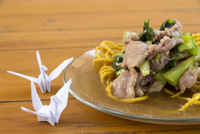 Close-up of meat salad on fried noodles in plate by origami at table