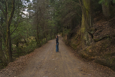 Side view of woman standing on dirt road amidst trees in forest
