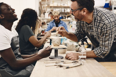 Cheerful mature man with work tool laughing while looking at student in art class