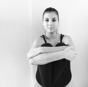 Portrait of confident beautiful woman hugging knees while sitting against wall