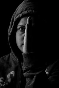 Close-up portrait of young woman wearing hoodie against black background