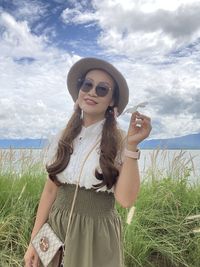 Young woman wearing sunglasses standing on field against sky