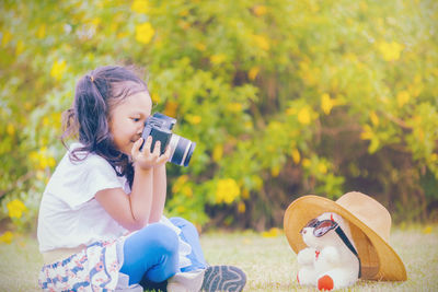 Cute girl holding camera while sitting on land