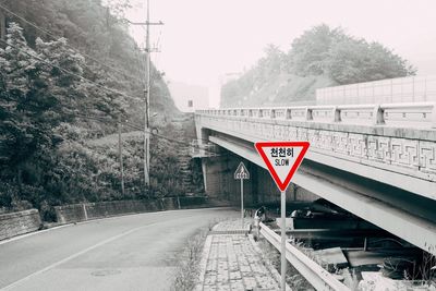 Road sign by railroad tracks against sky