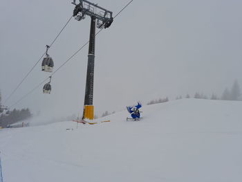 Close up of ski lift durino a snowfall with snow cannons belinda it ski on snow covered landscape