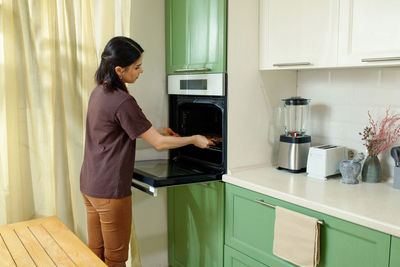 Side view of young woman standing in kitchen