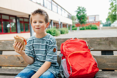 A schoolboy sits on a bench at recess and eats a healthy sandwich and an apple. snack while studying