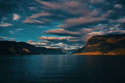 Scenic view of sea by mountain against dramatic sky