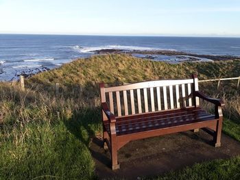 Empty bench on shore by sea against sky