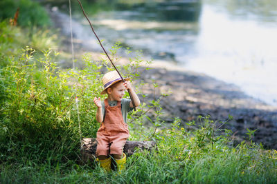 Cute boy with fishing rod sitting by river