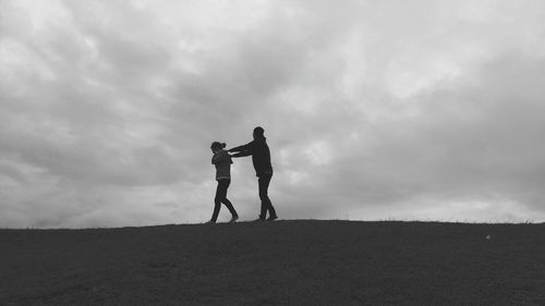 Low angle view of man and woman walking on hill against cloudy sky at dusk