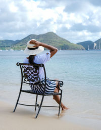 Rear view of woman sitting on chair at beach
