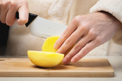 Close-up of female hands cutting fresh peeled potatoes tomatoes on cutting board at home kitchen
