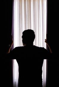 Rear view of silhouette man looking at window