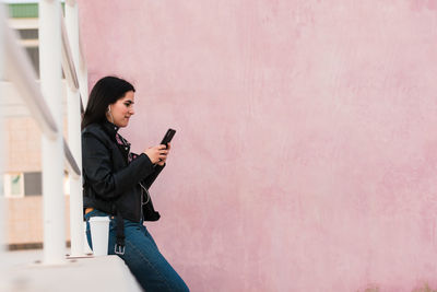 Young woman listen music and looks her smartphone in a pink background