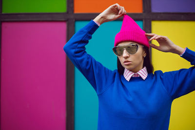 Fashionable brunette woman in a pink warm hat and sweater and sunglasses stands against background