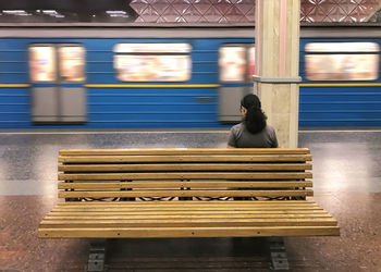 Rear view of woman sitting on bench by train at railroad station