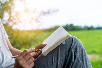 Midsection of woman reading book on field