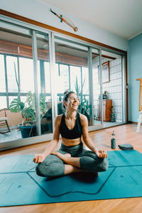 Happy young woman meditating on exercise mat at home