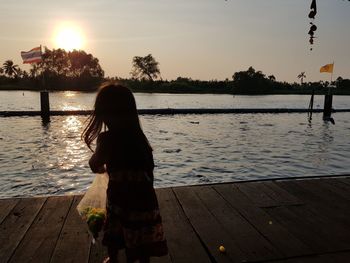 Rear view of woman standing on pier against sky during sunset