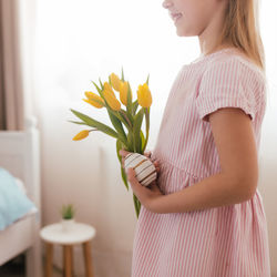 Side view of woman standing by flowering plants at home